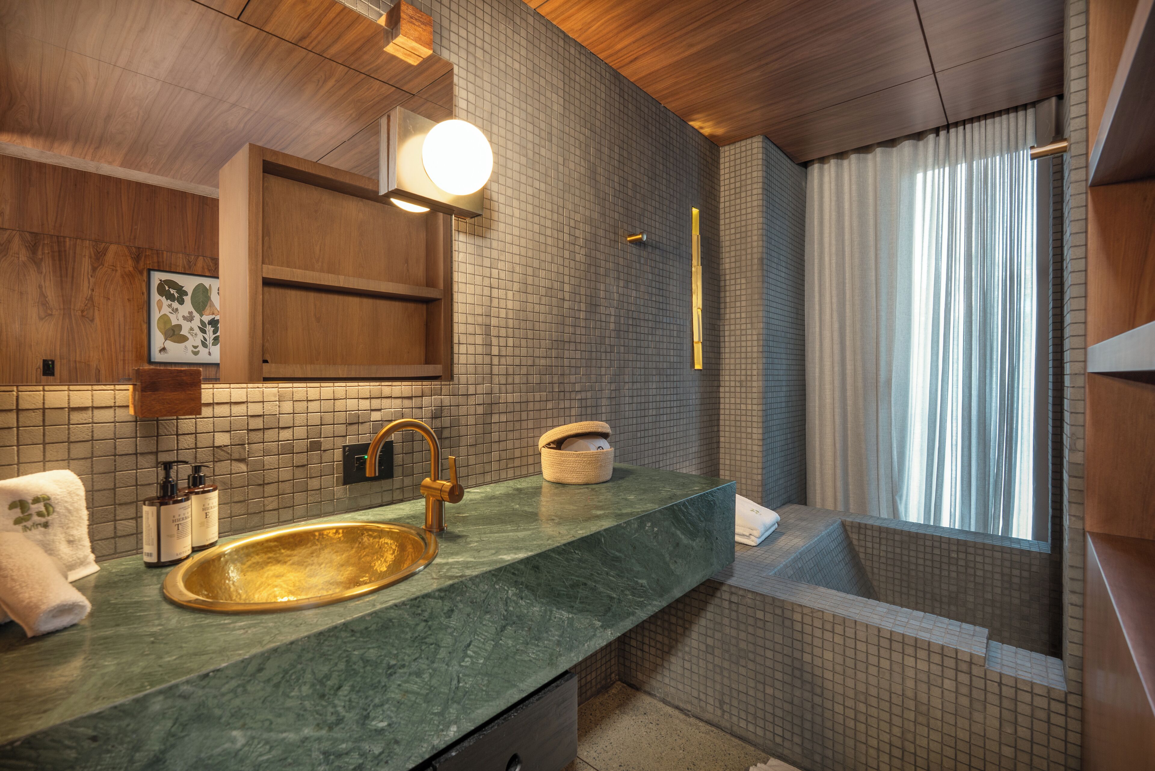 Un baño con lavamanos de mármol verde, techo de madera y un amplio ventanal con cortinas.