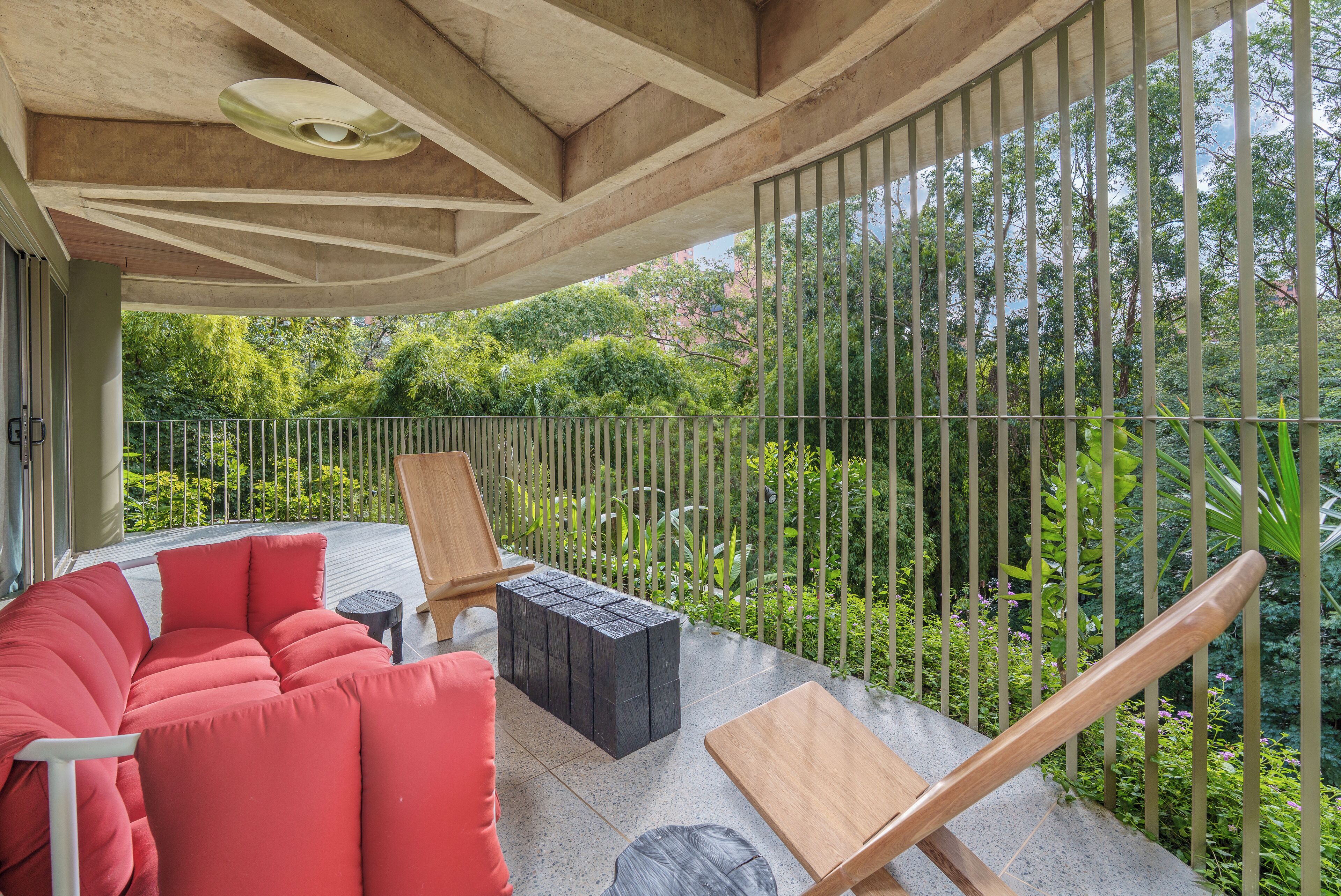 A covered outdoor seating area with a red sofa, a wooden table, and a black ottoman.