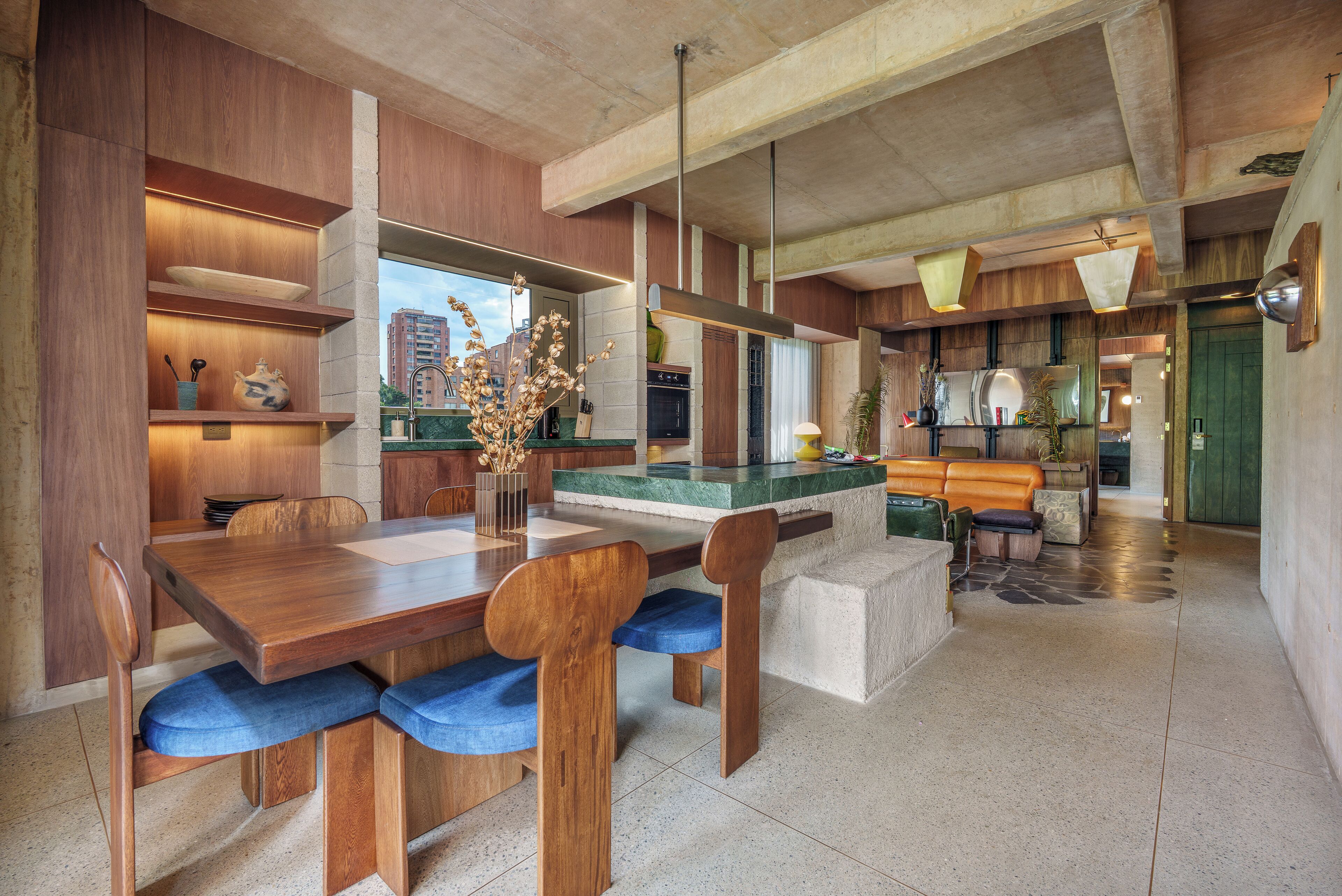 Une cuisine moderne avec un coin repas, comprenant une table en bois, des chaises rembourrées bleues et un îlot central intégré avec des sièges.