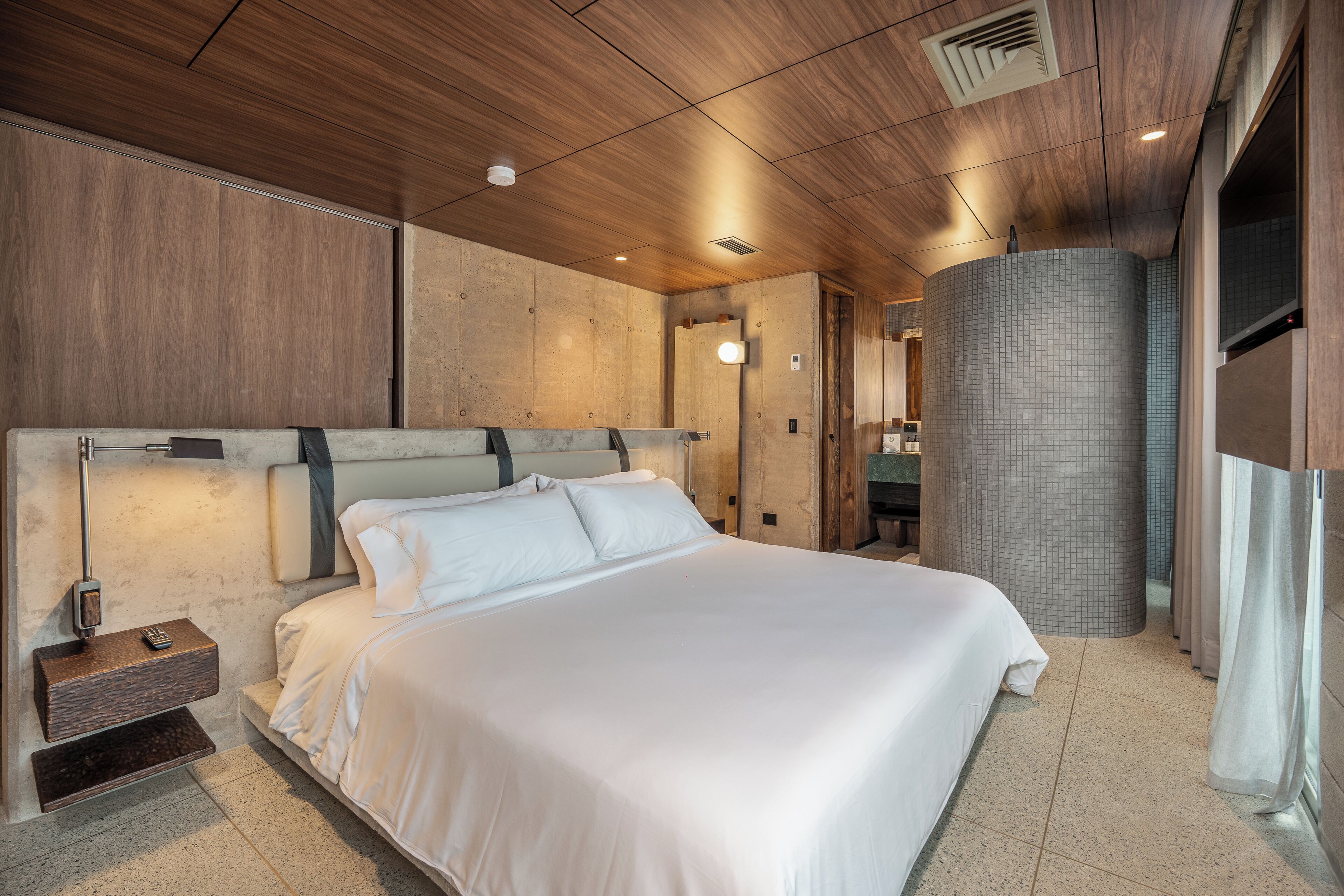 Camera d'albergo moderna con un letto grande, un comodino, una TV a parete e un bagno con doccia piastrellata.