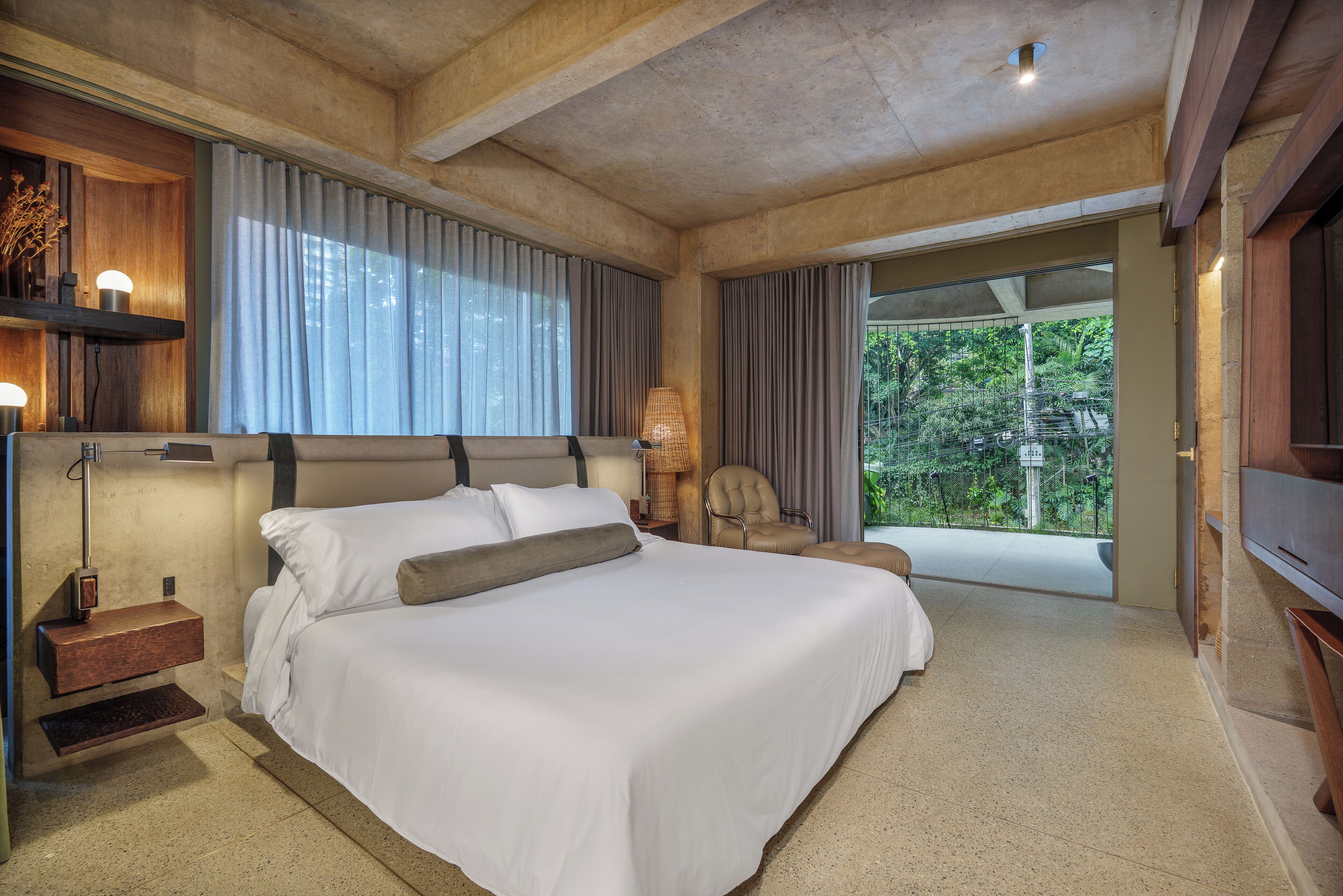A spacious bedroom with a large bed, a chair, a desk, and a window with curtains.