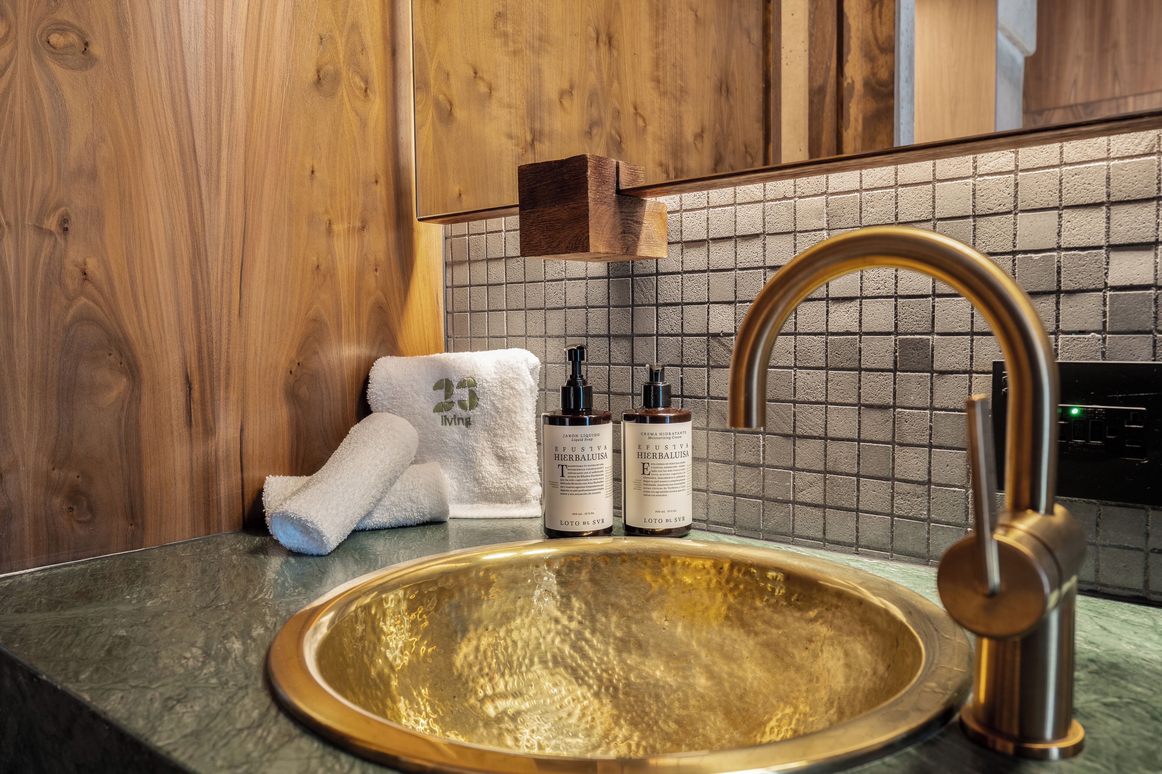 A bathroom with a wooden vanity, a gold sink, and toiletries.