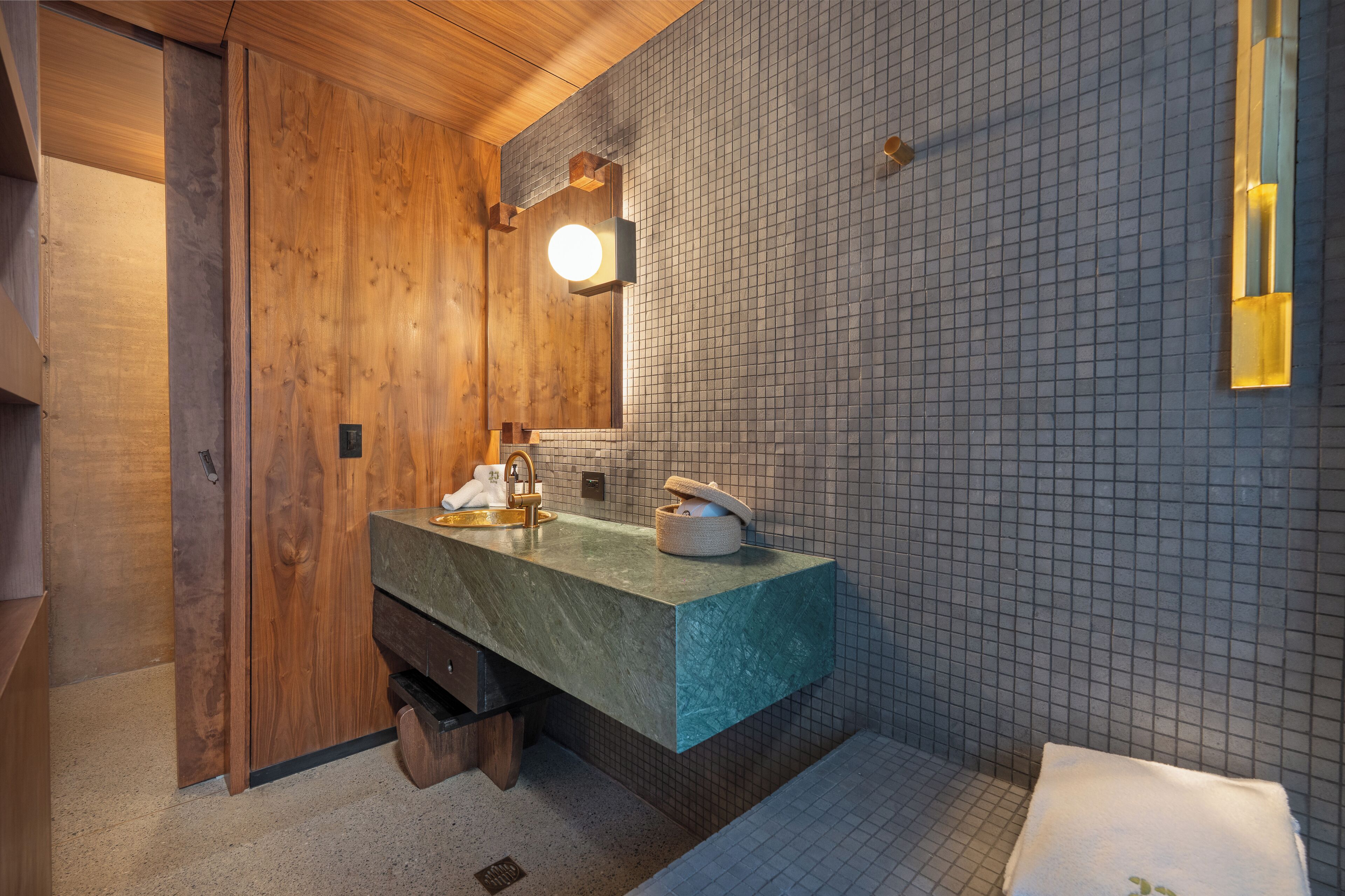 A bathroom with a wooden vanity, a sink with a green countertop, and a tiled wall.