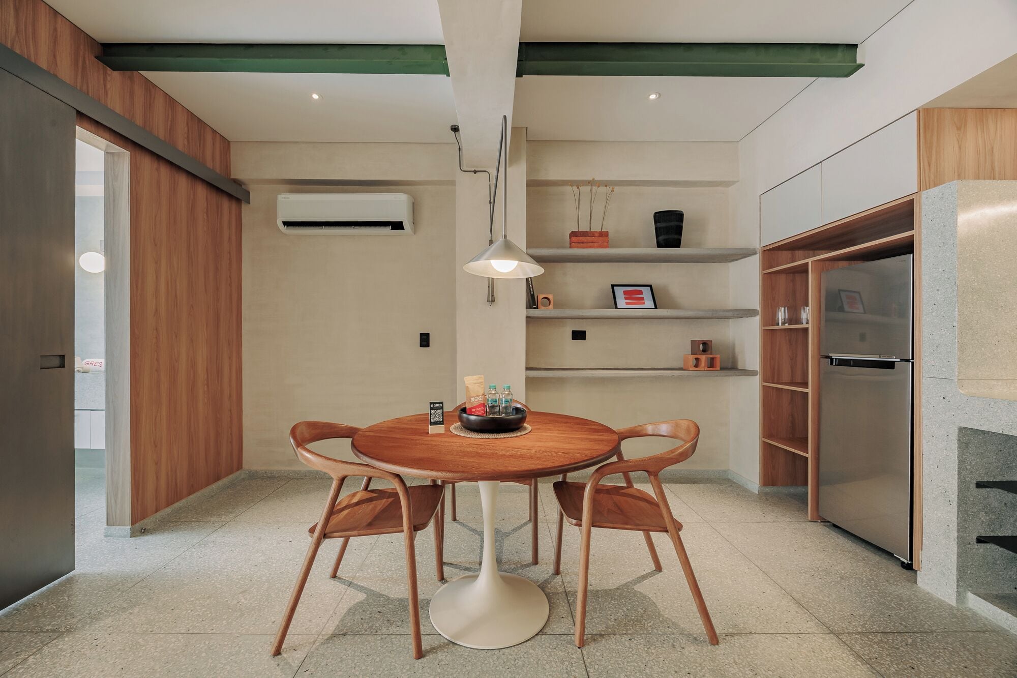 A modern kitchen with a round wooden table, two chairs, a built-in oven, and a wall-mounted air conditioner.