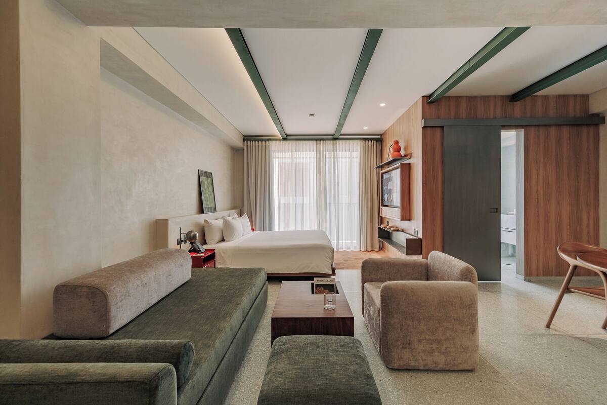 Una habitación de hotel moderna con cama, sofá, sillón y una mesita.