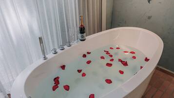 A bathtub with rose petals, a bottle of champagne, and a showerhead.