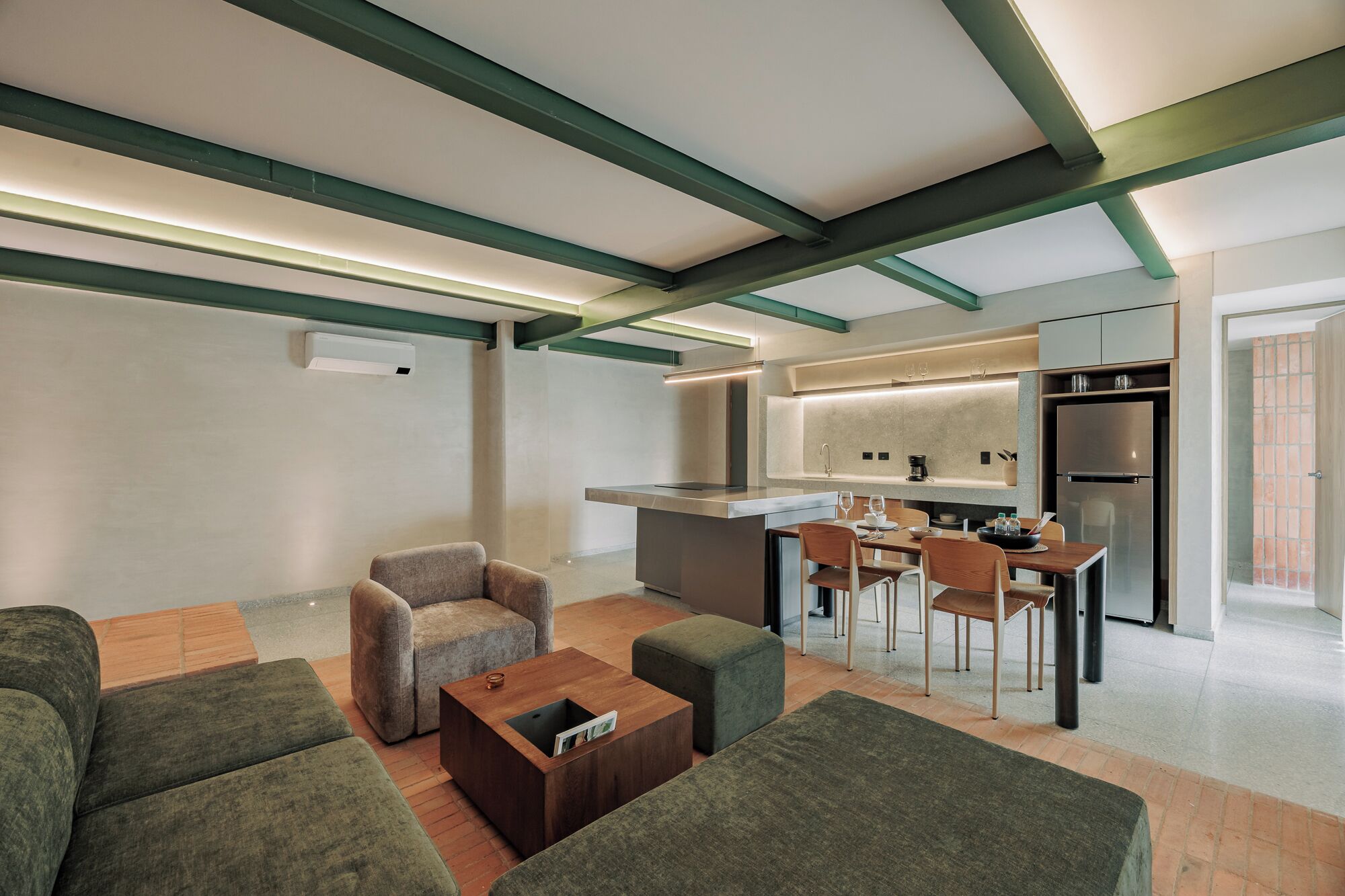 A modern living room with a sofa, ottoman, and coffee table, a kitchen with a refrigerator, and a dining area with chairs.