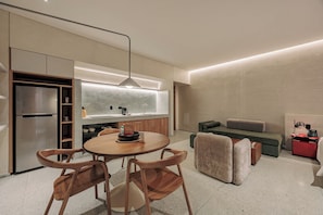 A modern kitchen with a built-in refrigerator, a dining table with chairs, a sofa, and a small red cabinet. - GRES Apartamentos (Medellín)