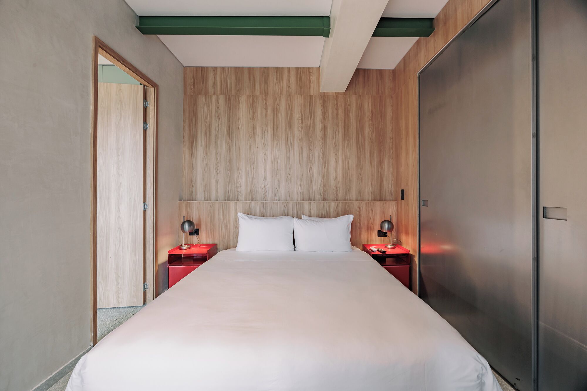 Een hotelkamer met een groot bed, houten paneelwanden, een deur en twee nachtkastjes met lampen.