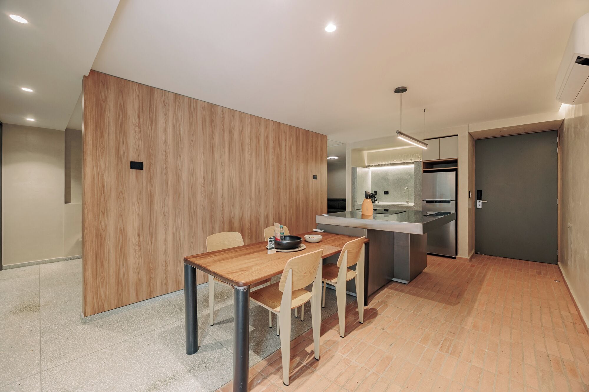 Una cocina moderna con horno empotrado y refrigerador, un comedor con mesa y sillas de madera, y una pared de acento de madera.