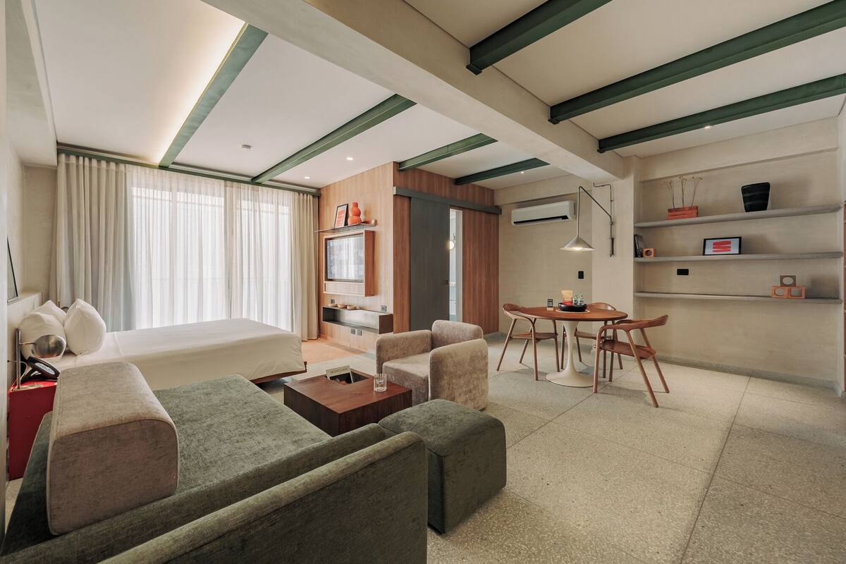Habitación de hotel moderna con cama, sofá, una mesa de centro y un área de comedor con sillas y una mesa.