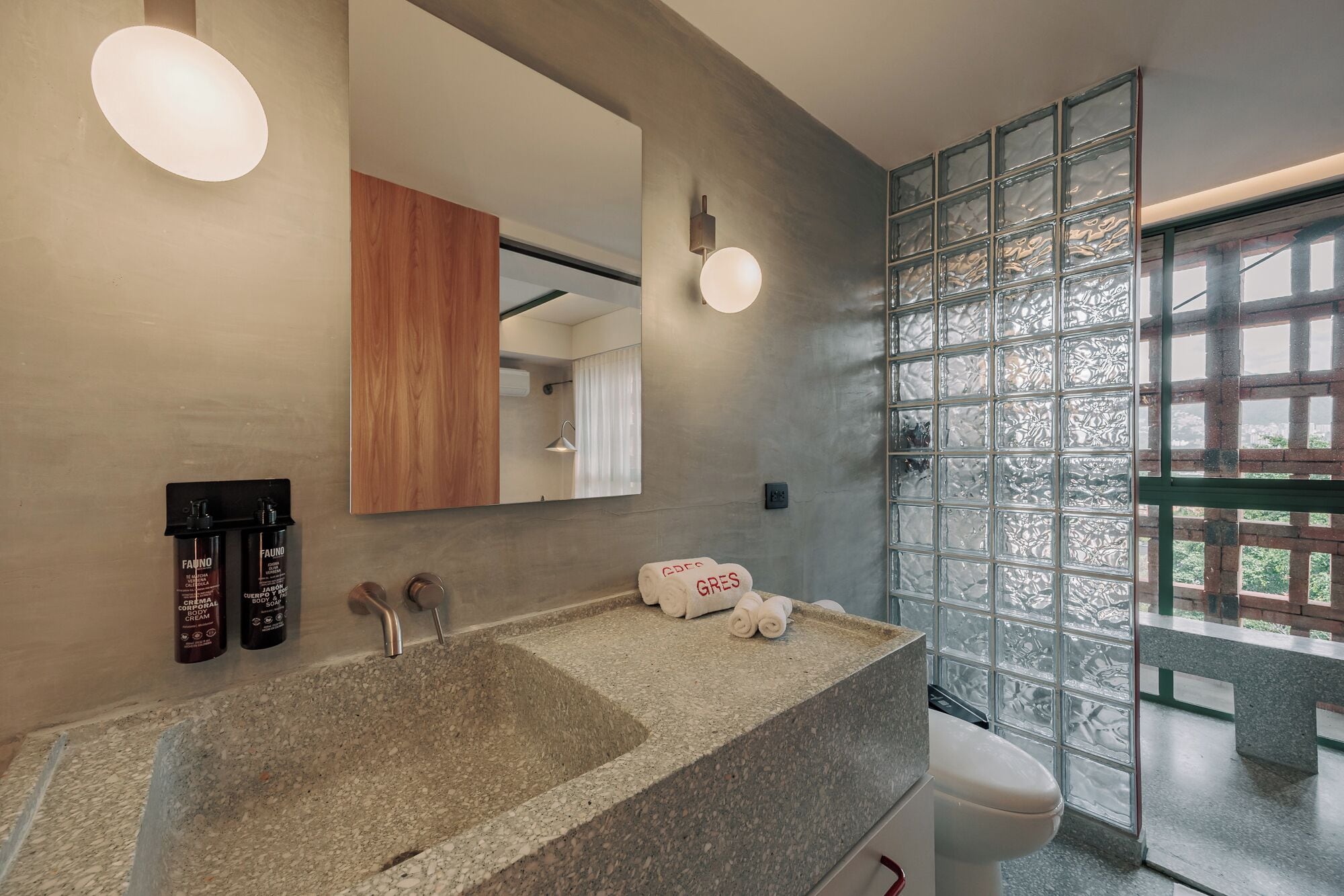 Un baño con lavamanos de granito, mueble de madera, espejo y mampara de vidrio con vistas.