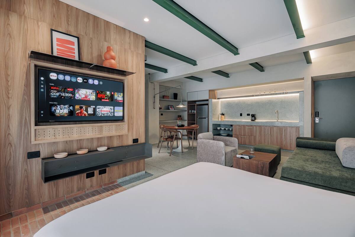 Una habitación de hotel moderna con un televisor de pantalla plana grande, un comedor, una kitchenette y una zona de estar con sofá y sillones.