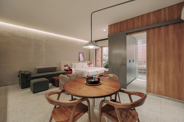 A modern hotel room with a dining area, a sofa, a bed, and a view of the outside. - GRES Apartamentos (Medellín)