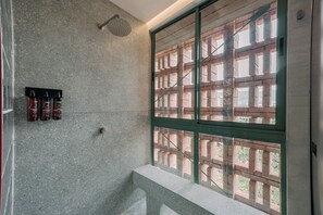A shower with a glass door, a window with a brick pattern, and three bottles of shampoo on the wall. - GRES Apartamentos (Medellín)