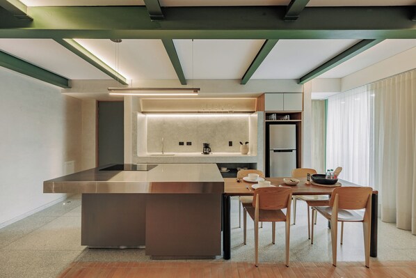 A modern kitchen with a central island, dining table, chairs, and a refrigerator. - GRES Apartamentos (Medellín)