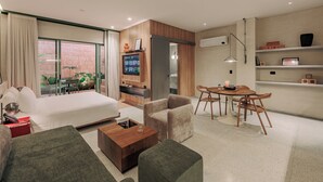 Une chambre d’hôtel moderne comprenant un lit, un canapé, une table basse, une télévision, un coin repas avec des chaises et un balcon agrémenté de plantes.