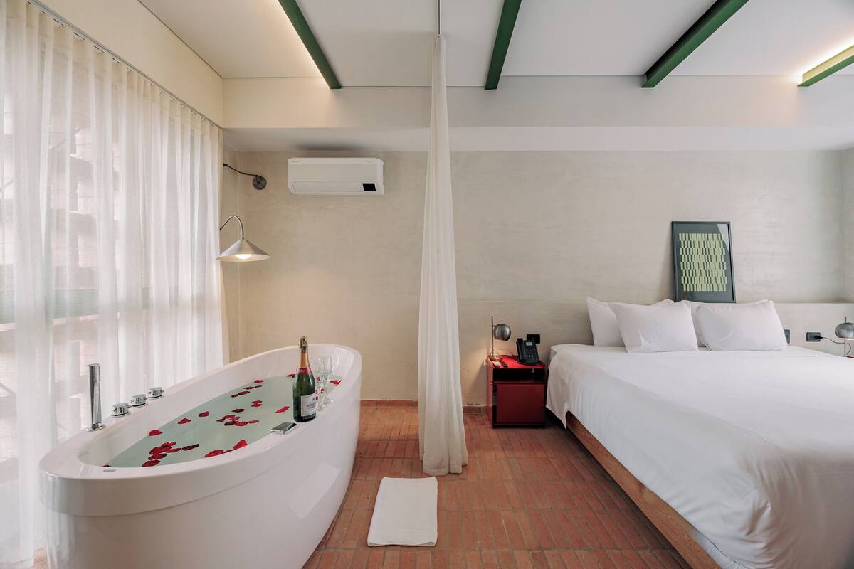 Una habitación de hotel moderna con bañera, cama, mesita de noche con teléfono y aire acondicionado de pared.