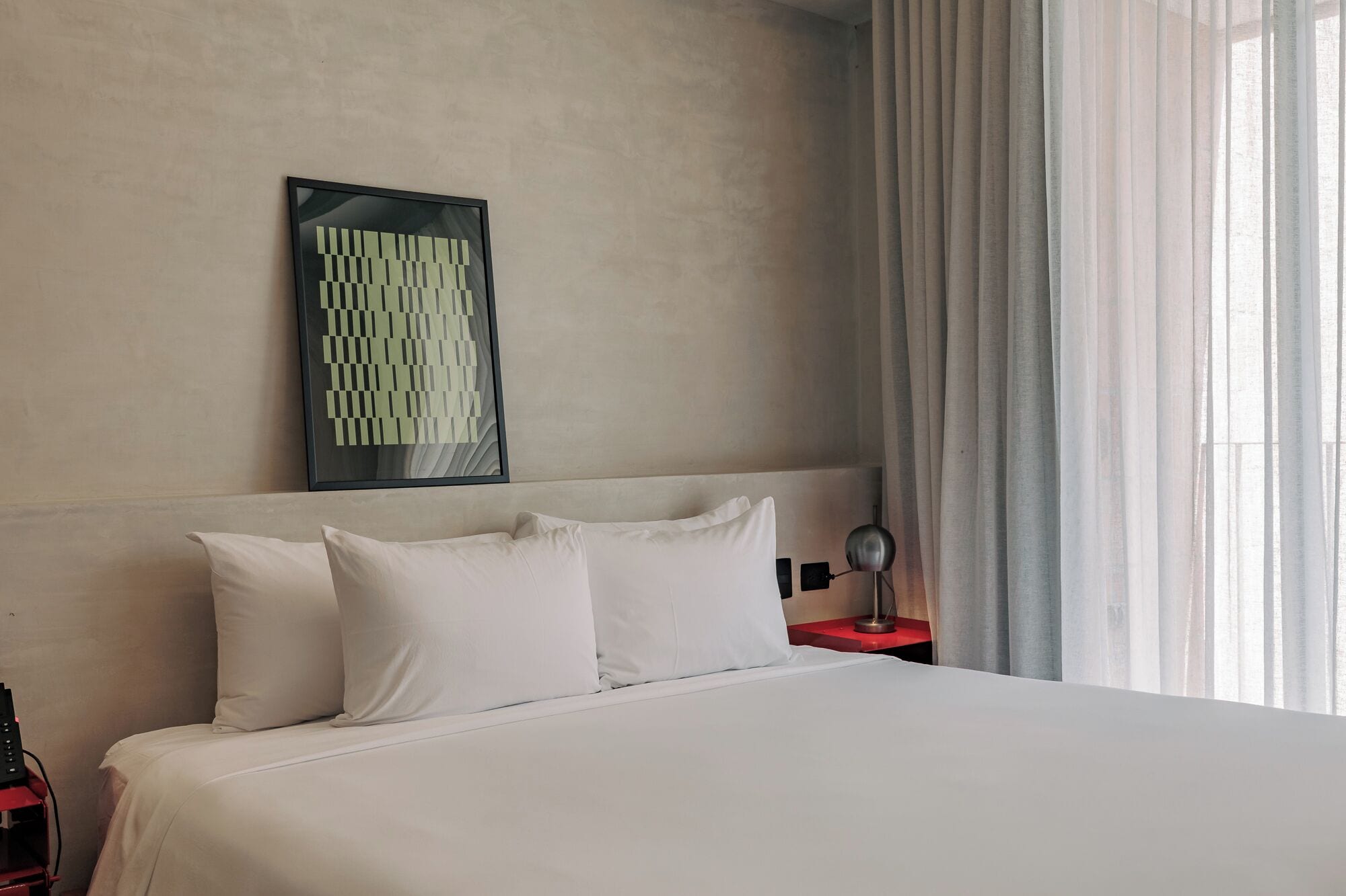 Una habitación de hotel con cama, mesita de noche, lámpara y un cuadro en la pared.