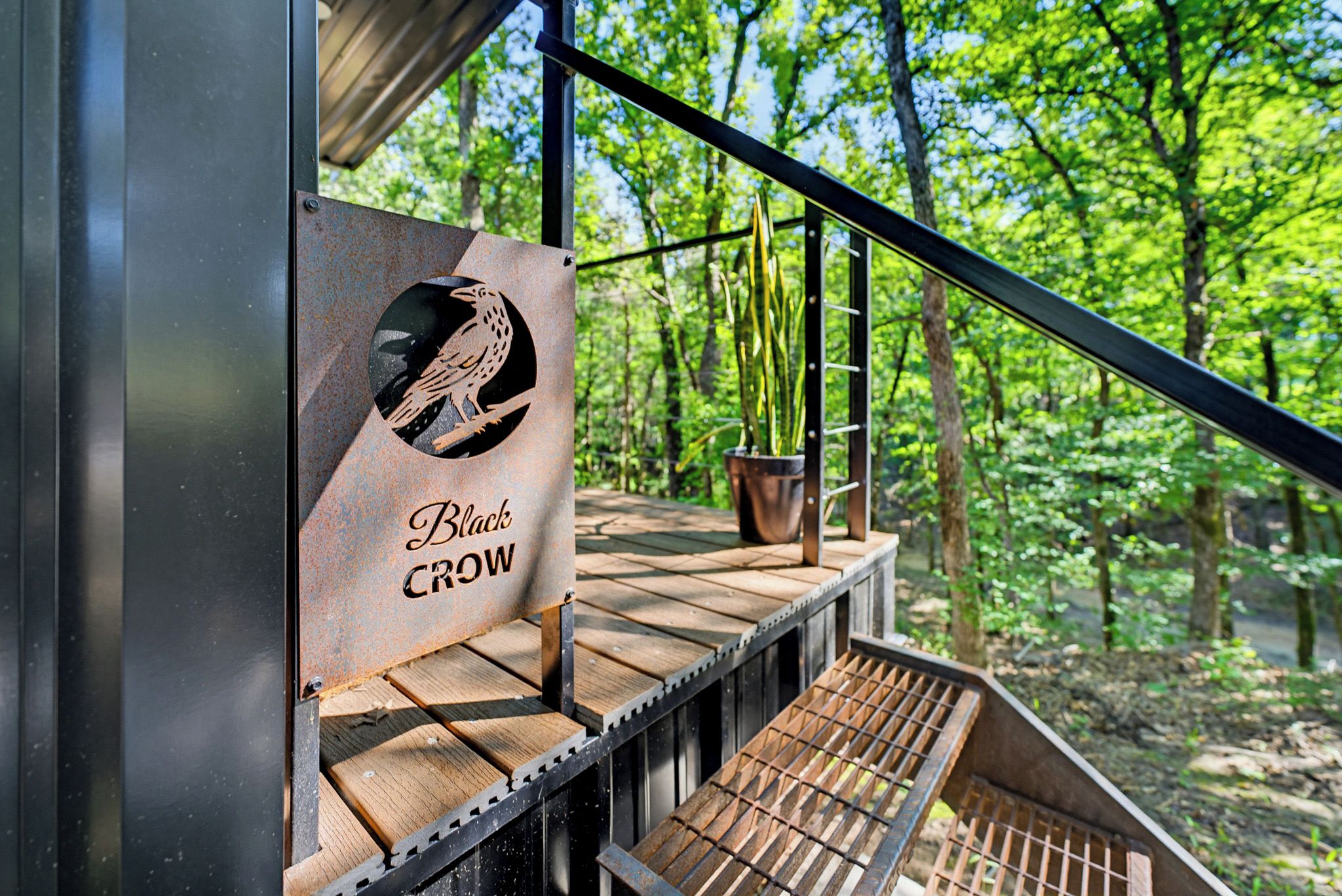 Une terrasse en bois avec une rambarde en métal, une enseigne indiquant « Black Crow », et un pot de fleurs.