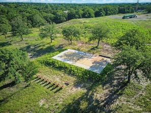 An aerial view of a green field with a concrete structure, surrounded by trees and vegetation. - Wooded Romantic Cabin near LBJ Grasslands - Book 1 or All 4 Cabins (Alvord)