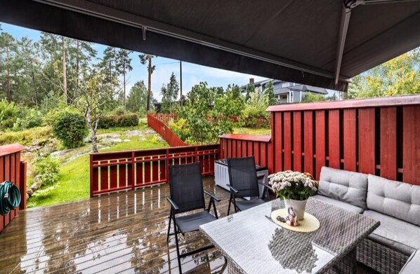 A covered outdoor area with a wooden deck, a red fence, and a seating area with a table and chairs. - Kazan Hotel Norge (Skien)