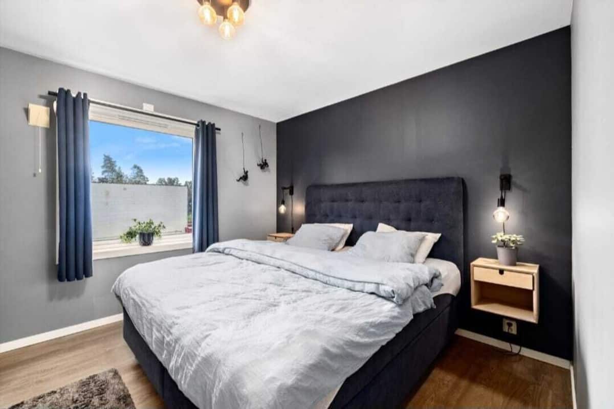 A modern bedroom with a large bed, a window with curtains, and bedside lamps.