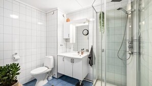 A modern bathroom with white tiles, a toilet, a sink with a mirror, and a glass-enclosed shower area. - Kazan Hotel Norge (Skien)