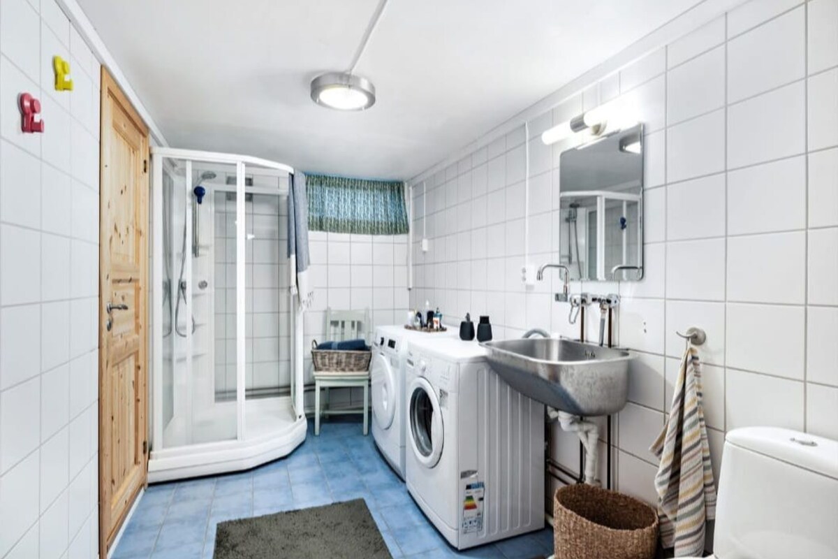 A compact, modern bathroom with a built-in washing machine, a shower enclosure, and a sink.