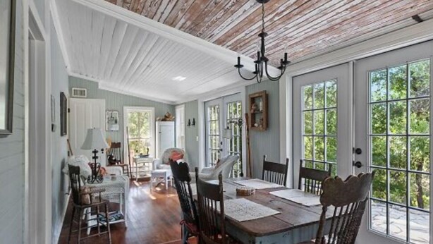 Comedor con mesa y sillas de madera, ventanas grandes y techo con vigas a la vista.