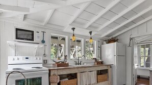 Una cocina con armarios blancos, encimera de madera y horno integrado. Hay cestas colgantes y una ventana con vistas a zonas verdes.
