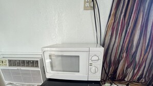 A white microwave on top of a black refrigerator in a kitchen with a wooden floor and a power outlet on the wall. - WESTERN STATESINN (San Miguel)