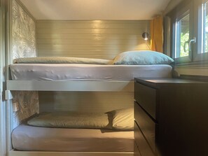 Cozy retreat with a bunk bed arrangement, featuring a bedside table and lamp, and a window with a view of lush greenery.