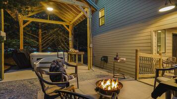 Un patio al aire libre con una chimenea, asientos y una zona cubierta con un jacuzzi.