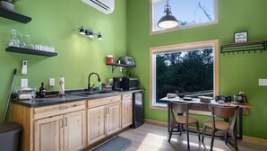A kitchen with wooden cabinets, a black countertop, a window with a view of trees, and a dining area with a table and chairs. - 2 Level Cabin w/Hot Tub & Fireplace. 1.5 Bathrooms, 2 Queen Beds (Ashland)