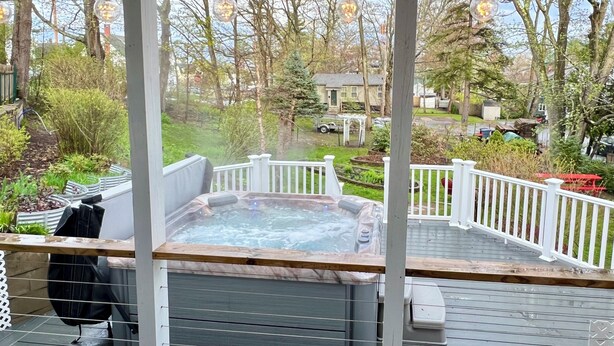 Eine überdachte Terrasse im Freien mit Whirlpool, Holzgeländern und Lichterketten.