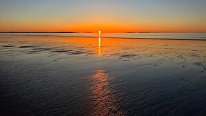 Ein Strand bei Sonnenuntergang mit ruhiger See und blauem Himmel.