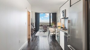 A modern kitchen with a large refrigerator, a dining area with a table and chairs, and a view of the city through large windows.