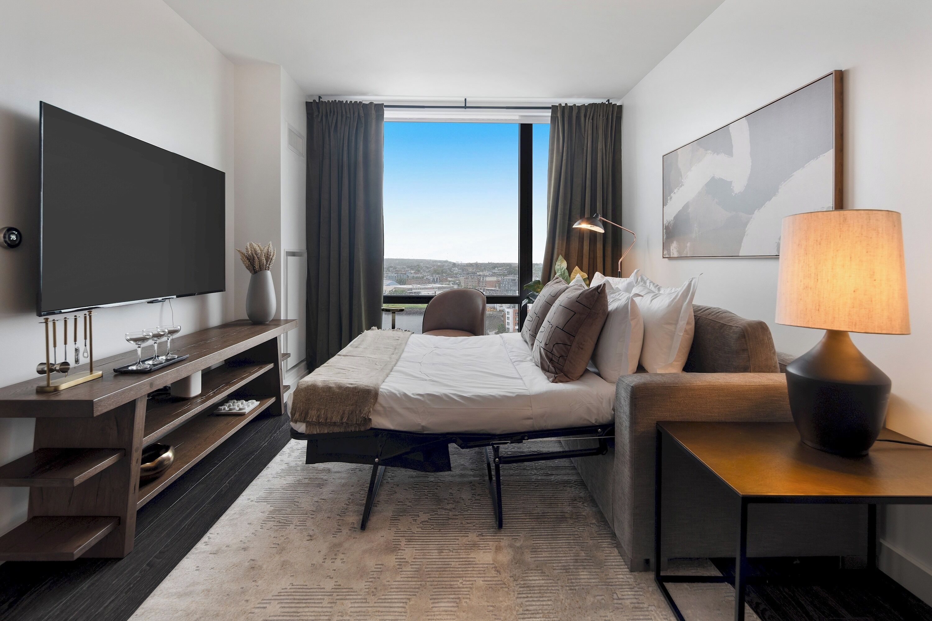 Habitació d'hotel moderna amb un llit gran, una televisió, escriptori i vista a la ciutat.