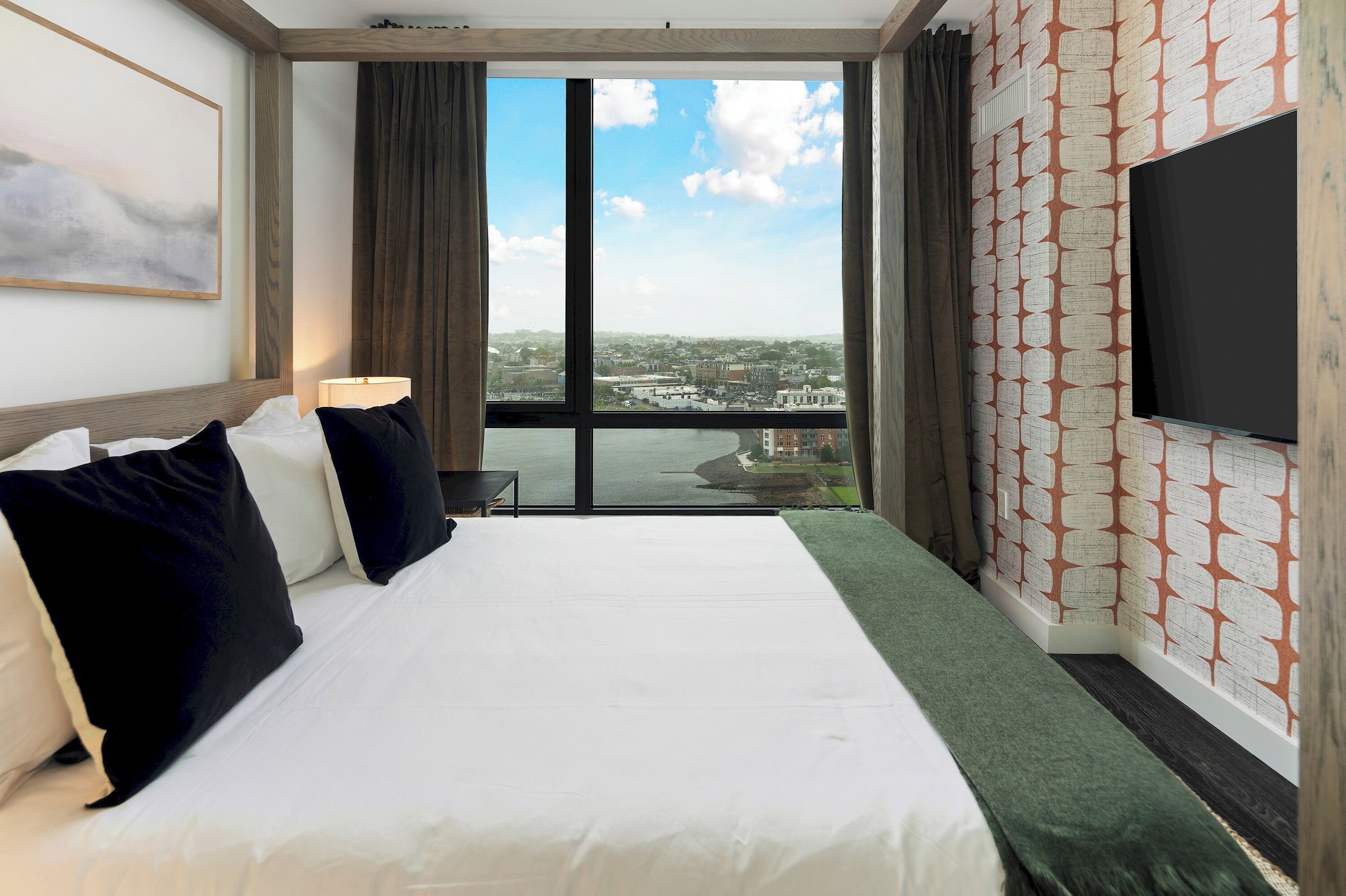 Habitación de hotel con una cama grande, un televisor de pantalla plana, una ventana con vista a la ciudad y un papel tapiz estampado.