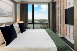 Une chambre d’hôtel avec un grand lit, un téléviseur à écran plat, une fenêtre donnant sur la ville et un mur décoré d’un motif.