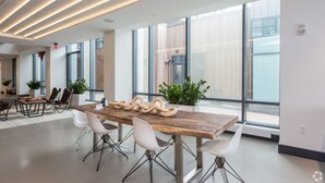A modern conference room with a wooden table, white chairs, and large windows.