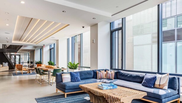 A modern living area with a blue sofa, wooden coffee table, and large windows.