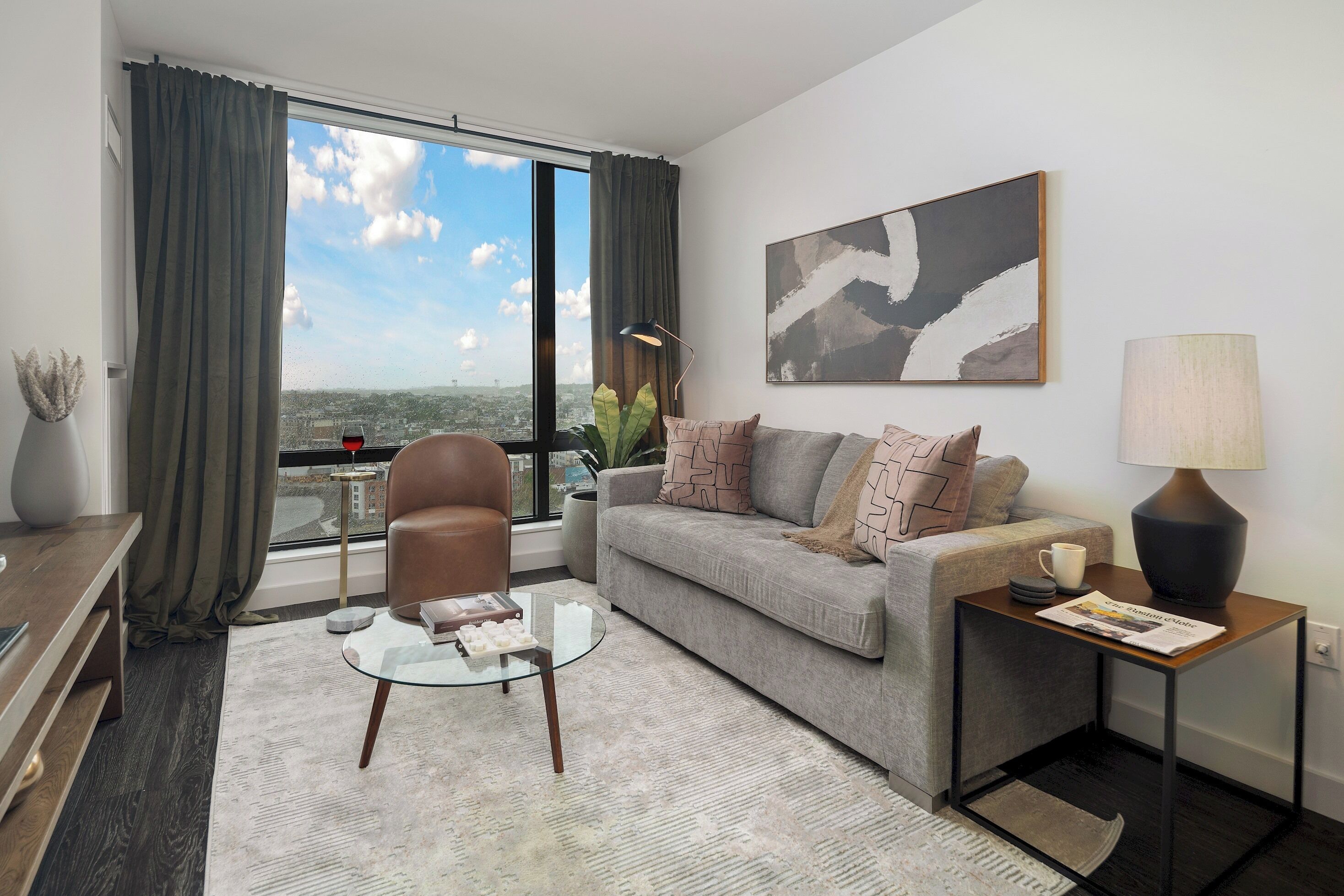 Ein modernes Wohnzimmer mit Sofa, Ohrensessel, Couchtisch und Blick auf die Stadt durch große Fenster.