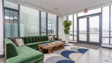 A modern lobby with a green sofa, a wooden coffee table, and large windows offering a view of the city.