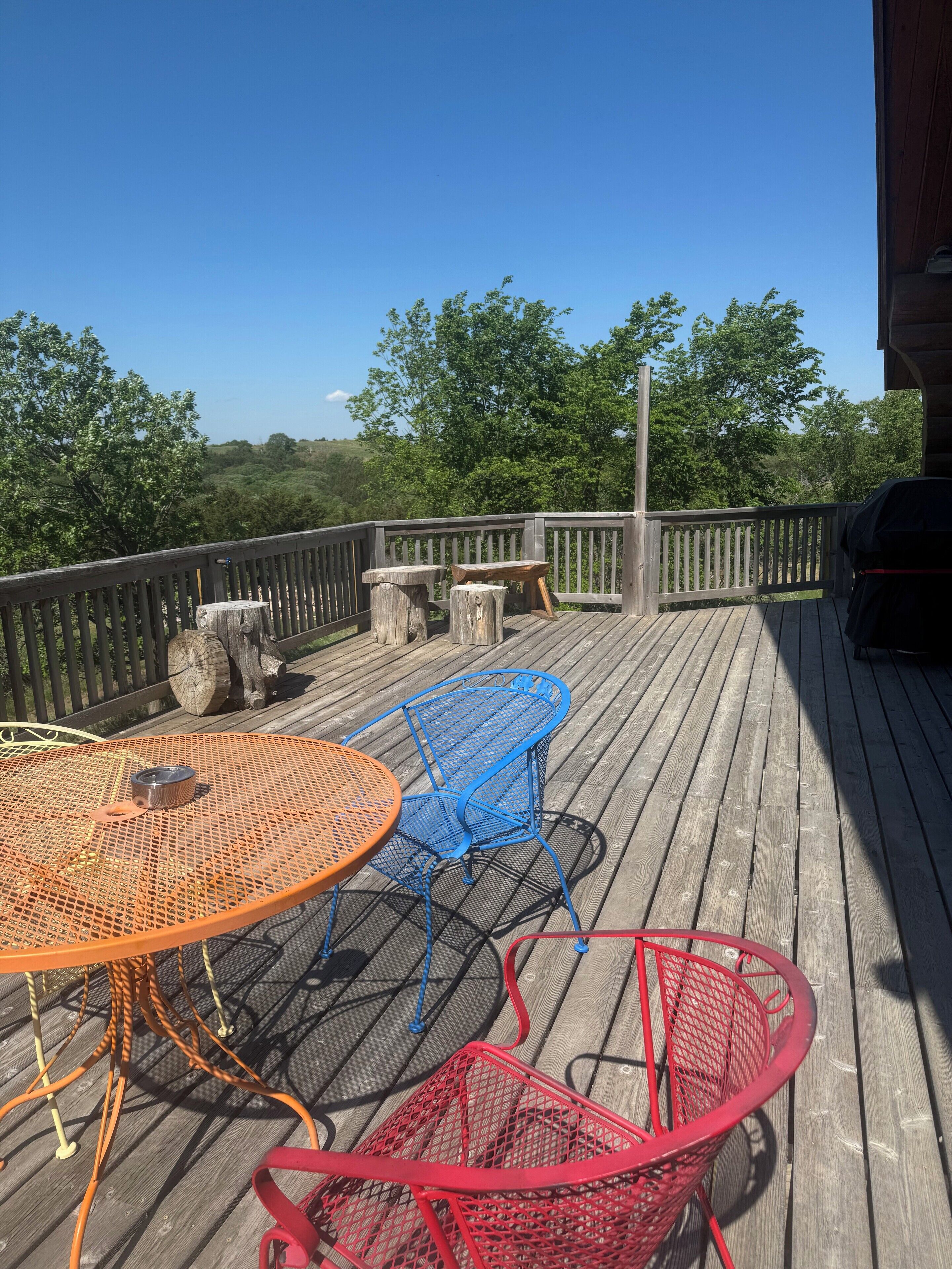 A wooden deck with a round table and two chairs, a red basket, and a barbecue grill.
