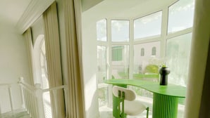 A room with a green desk, a white chair, and a view of a building through large windows. - La Petite Maison Charme en Bord de mer (Carthage)
