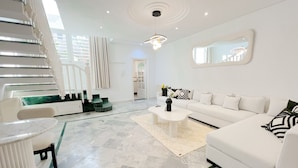 A modern living room with a white sofa, a coffee table, and a staircase with a glass railing. - La Petite Maison Charme en Bord de mer (Carthage)