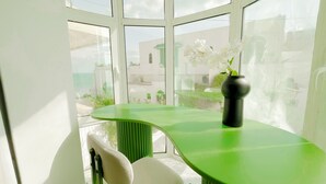 A room with a green table and a white chair, a vase with flowers, and a view through large windows. - La Petite Maison Charme en Bord de mer (Carthage)