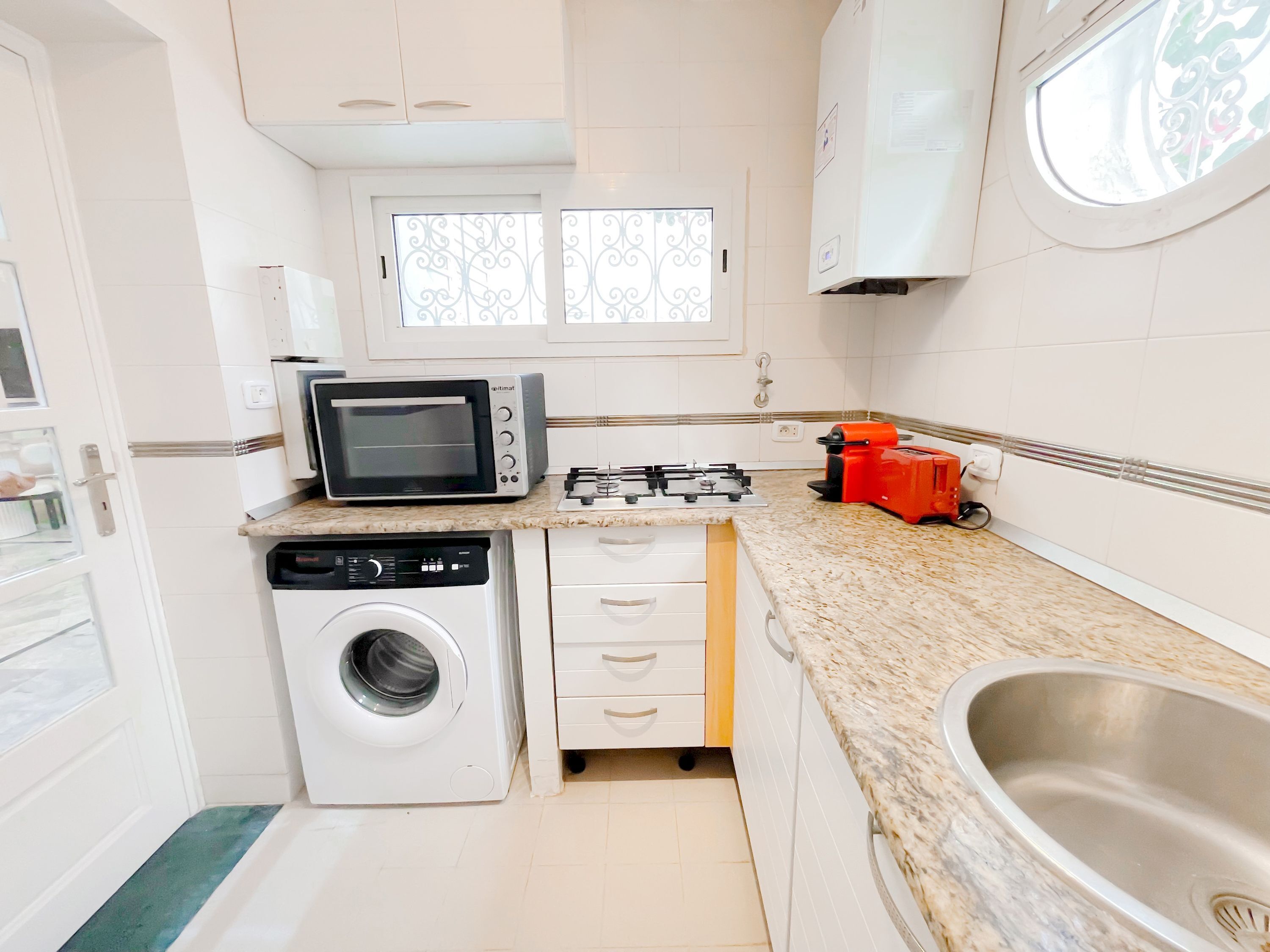 A compact kitchen with a microwave, gas stove, washing machine, and a sink.